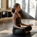 A woman meditates in a peaceful yoga pose indoors, embracing wellness and relaxation.