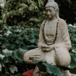 A tranquil Buddha statue surrounded by lush green lotus leaves in a garden, symbolizing peace and serenity.