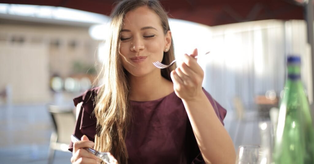 A woman savoring her meal with a smile, dining outdoors in a pleasant setting.