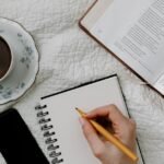 Handwriting on notebook with open book and coffee in bed. Perfect cozy setup for reading or studying.
